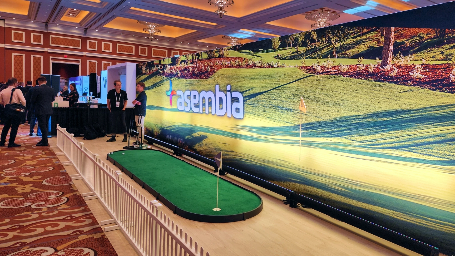 Asembia's booth at an industry event, featuring a golf-themed display with a putting green.