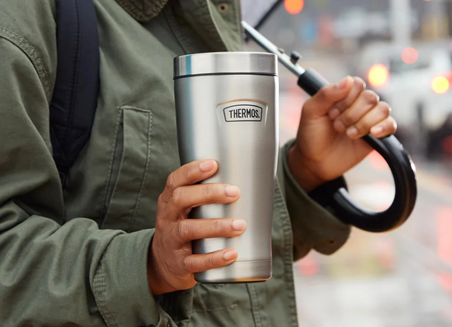 hand holding umbrella and thermos silver cup