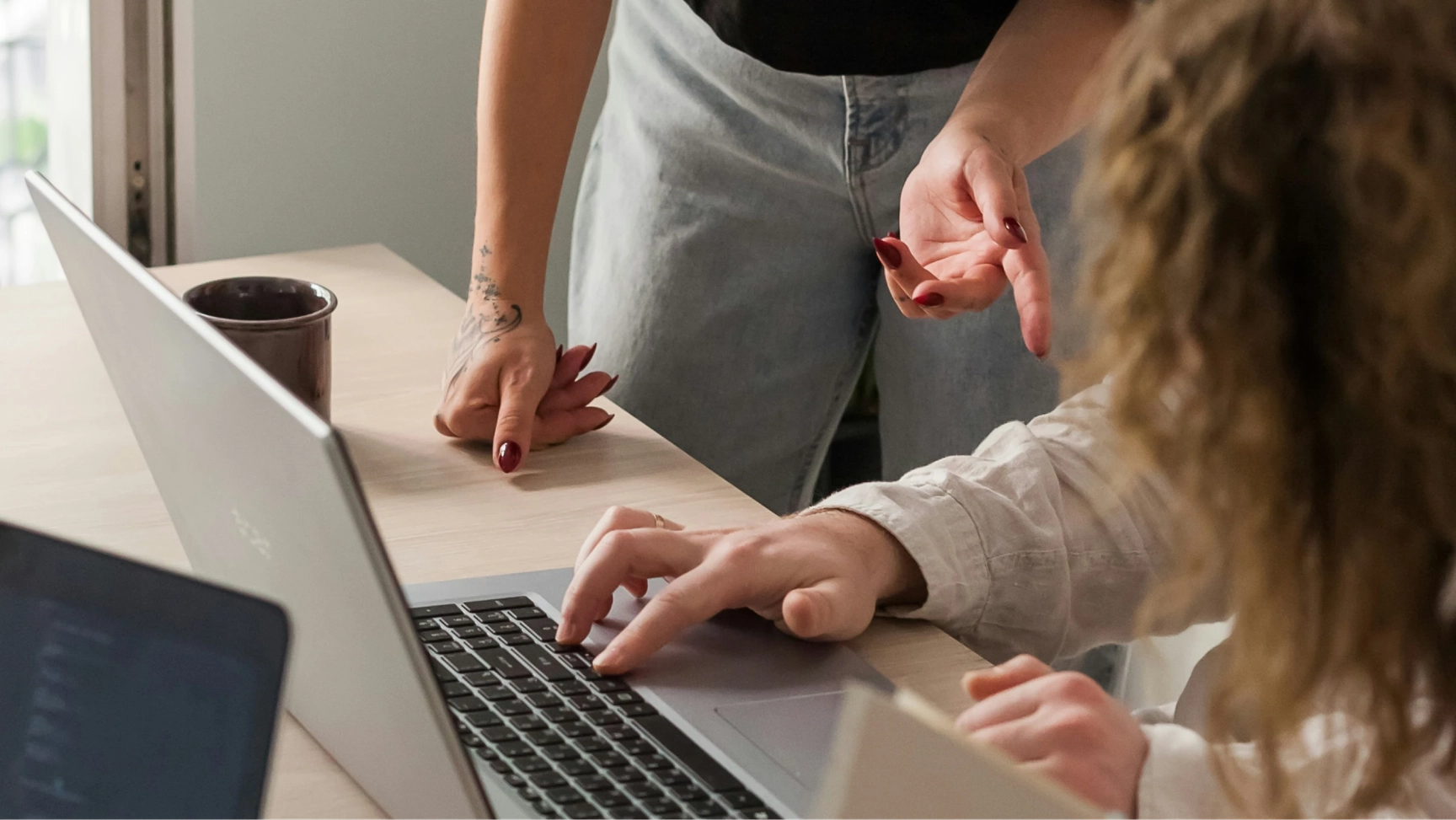 Team collaboration at desk with laptop, coworkers discussing project and analyzing data on screen