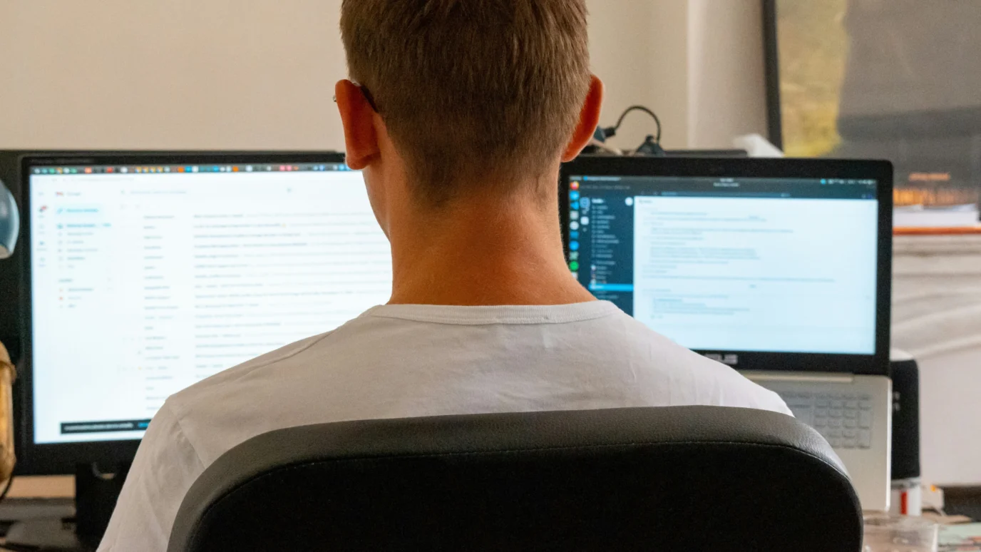 Rear view of a developer or content strategist sitting at a desk with two monitors, one displaying a Content Management System (CMS) dashboard and the other showing code, emphasizing back-end integration and administrative control.