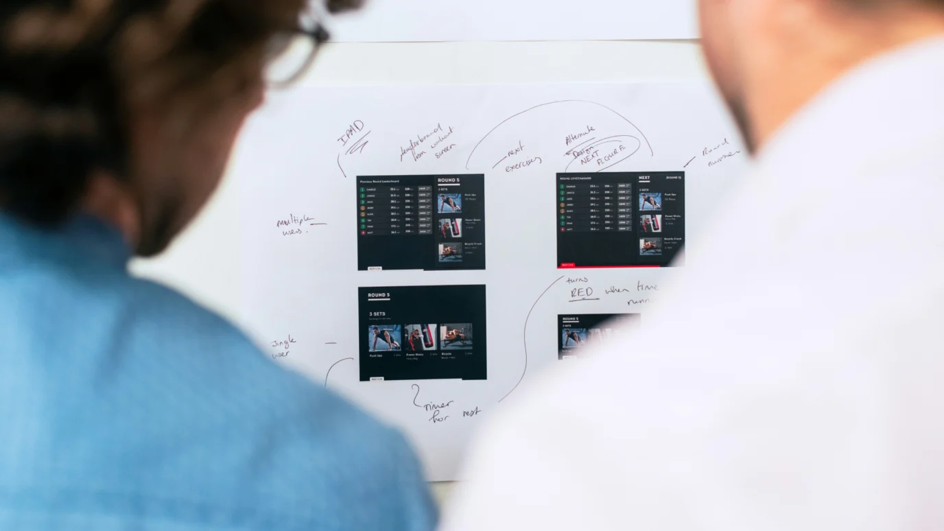 UX research and strategy session: two designers collaborating on wireframes, user interface (UI) screens, and handwritten feedback during a product design review.