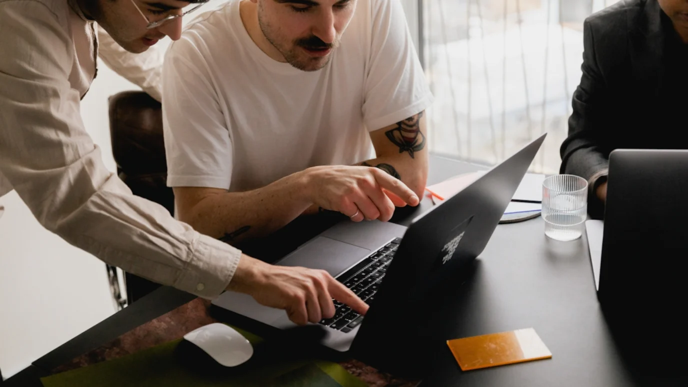 Product design team collaborating on a laptop during a UX strategy meeting, pointing at the screen and keyboard to review user experience (UX/UI) design or research data.