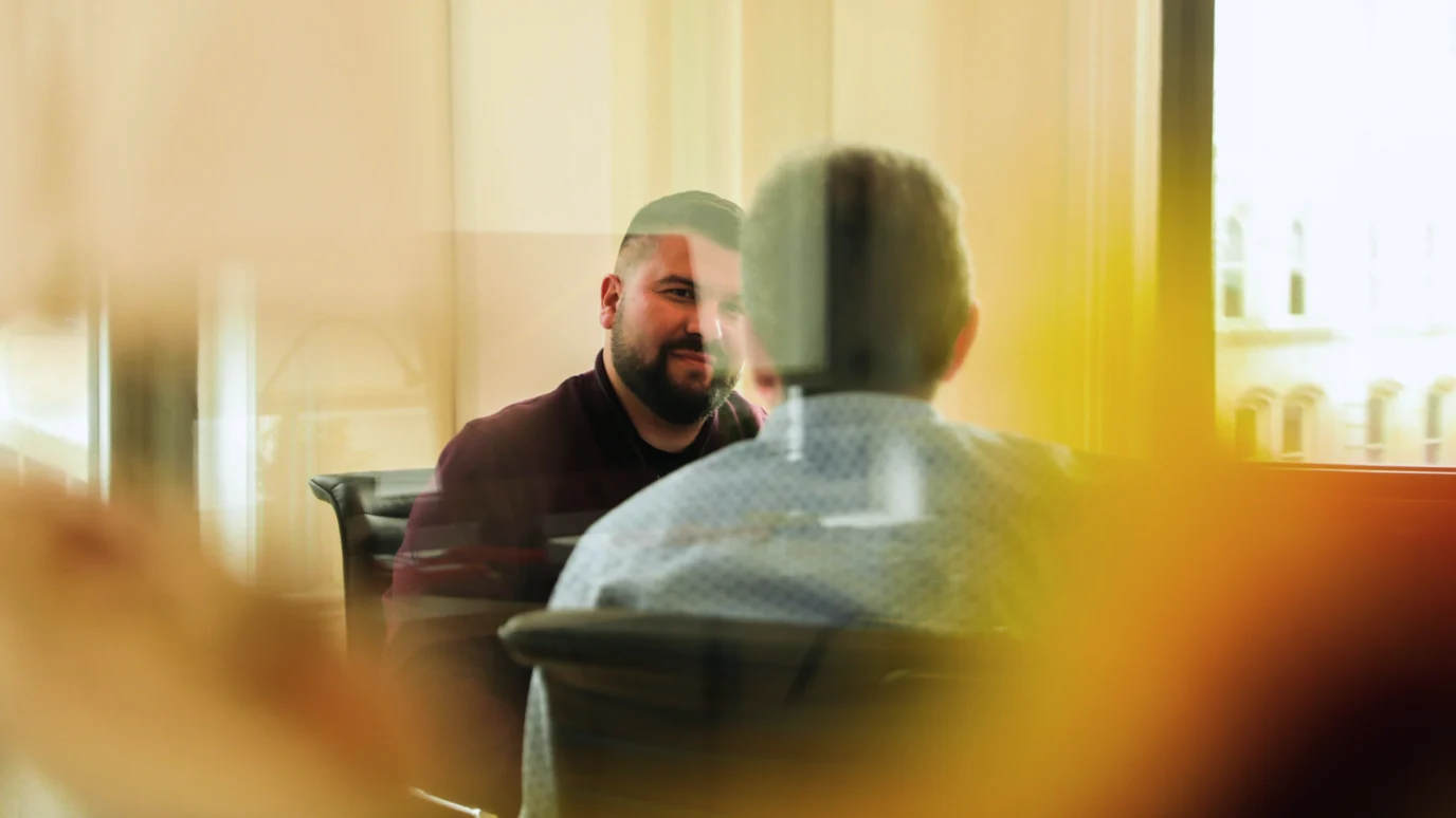 Professional business meeting or user interview in a modern office, showing two men seated across a table, focusing on collaboration and qualitative research.