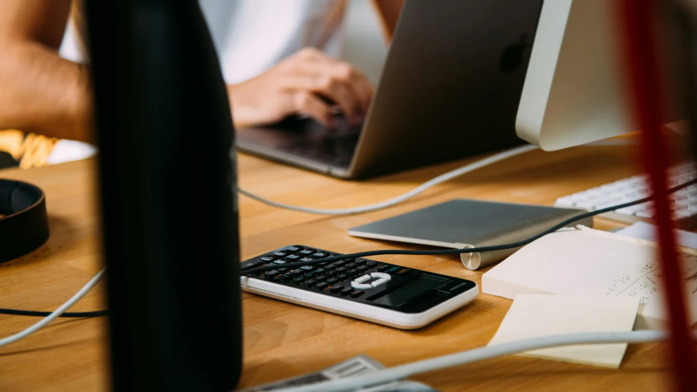 Close-up of a scientific calculator and handwritten notes on a wooden desk, symbolizing a startup founder or team working on performance metrics, forecasting, and financial models for scaling.