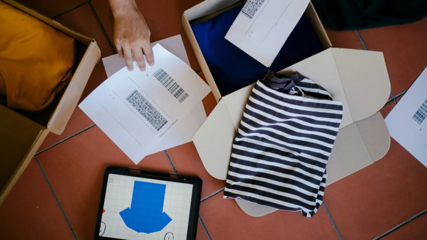 Overhead view of eCommerce order fulfillment process including apparel packaging, barcode shipping labels, and a digital tablet for inventory tracking.