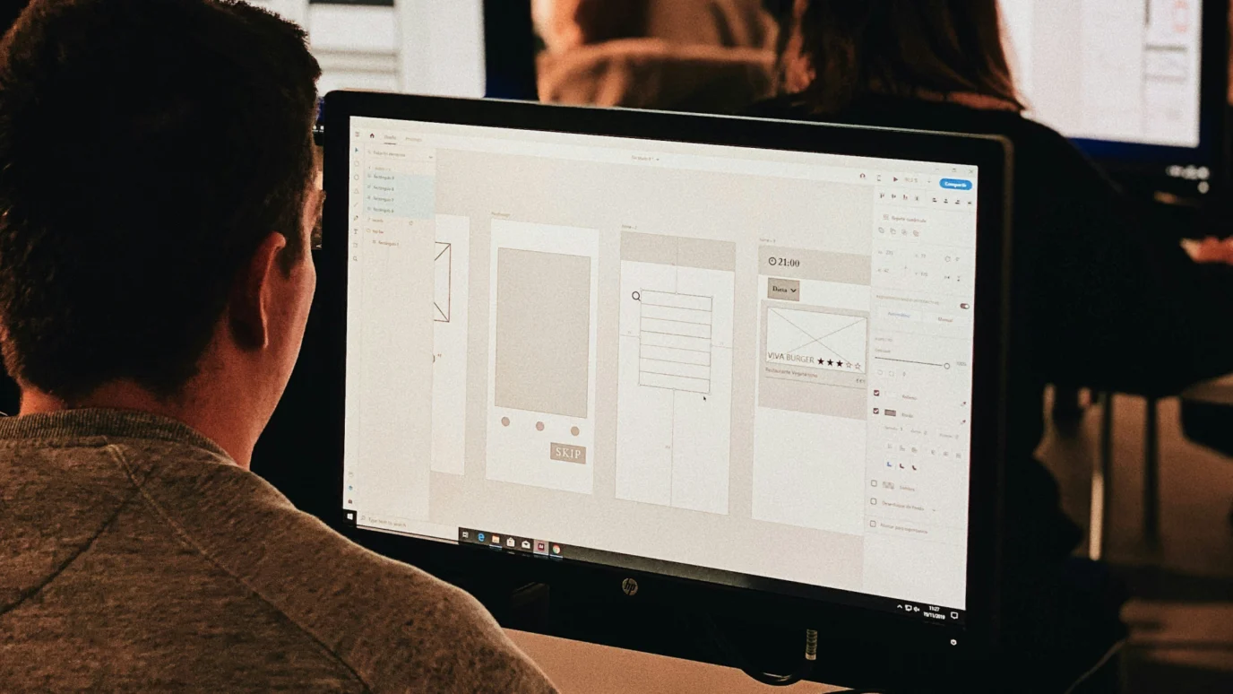 Designer working on a digital wireframe on a desktop monitor.