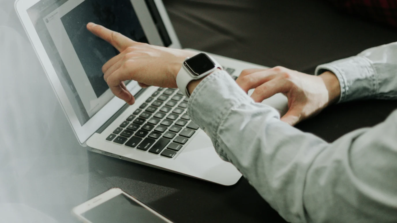 Person wearing a smartwatch pointing at a document on a laptop screen.
