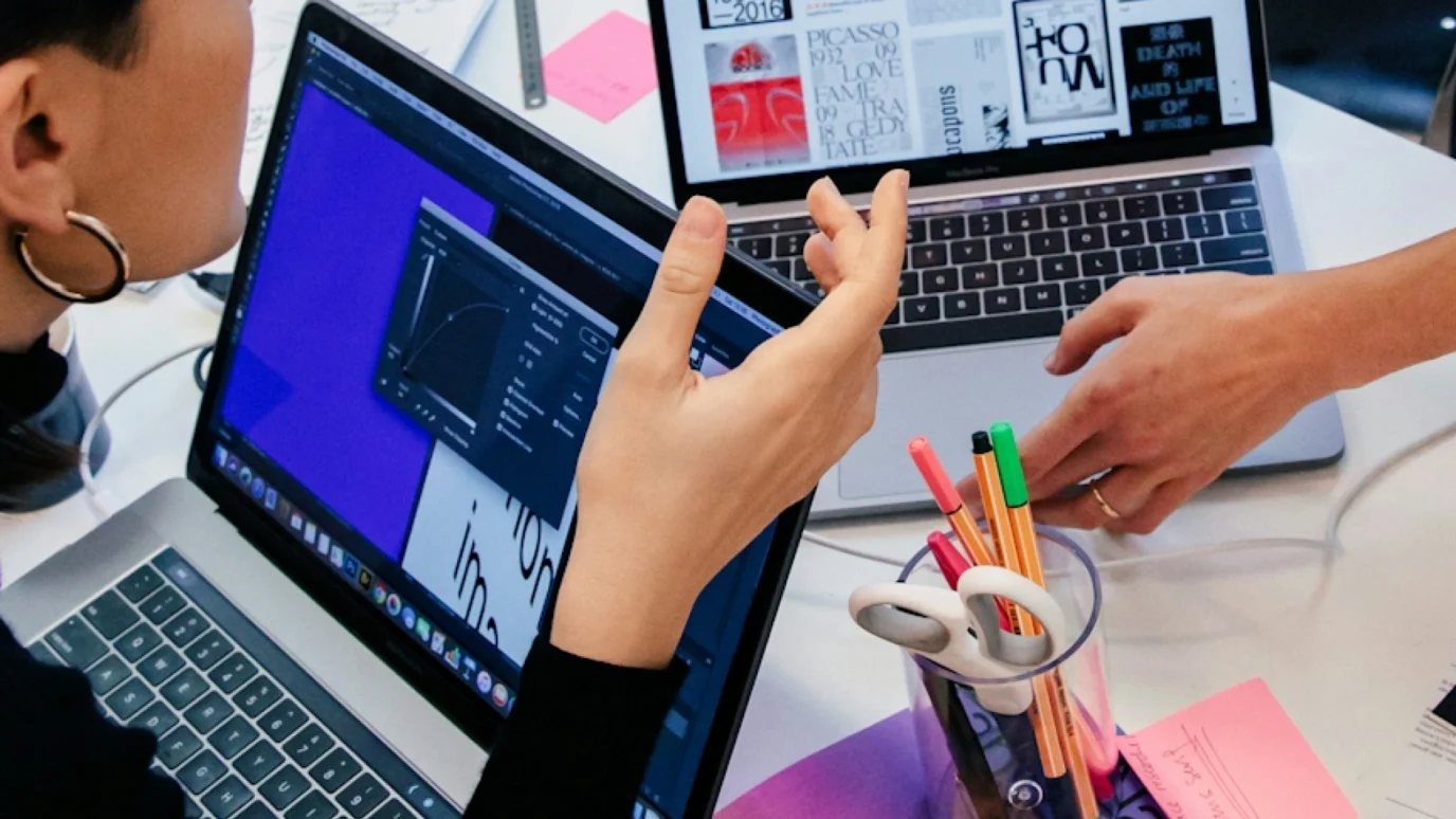 Two designers looking at visual design inspiration and graphics software on laptops.